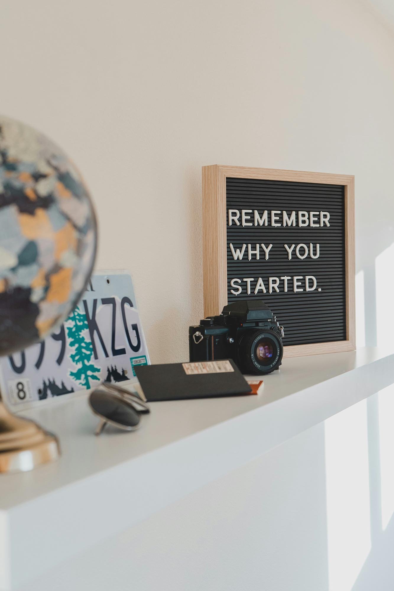 Shelf with camera, globe and sign that says remember why you started