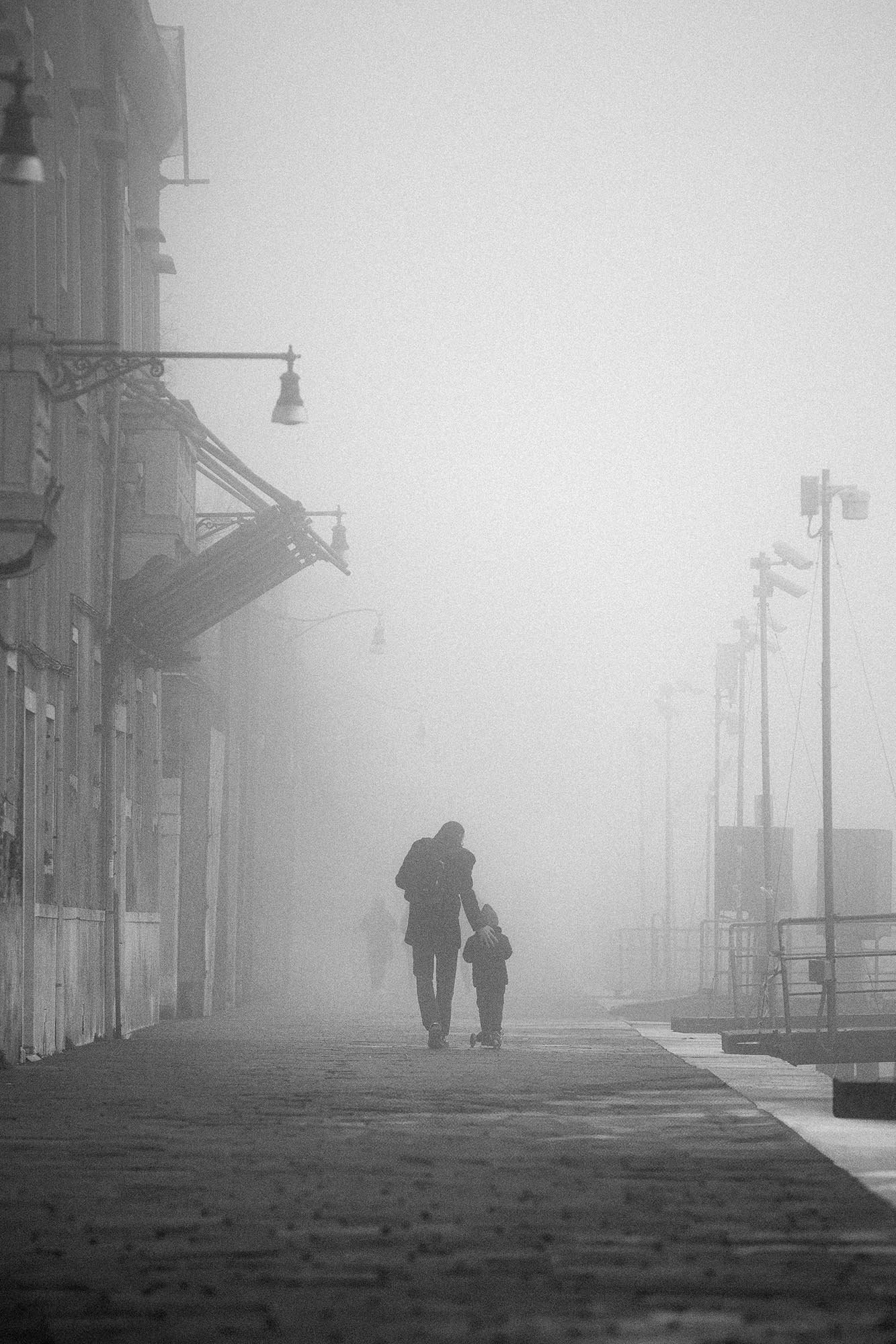 Black and white street photo of a parent and child walking in the fog